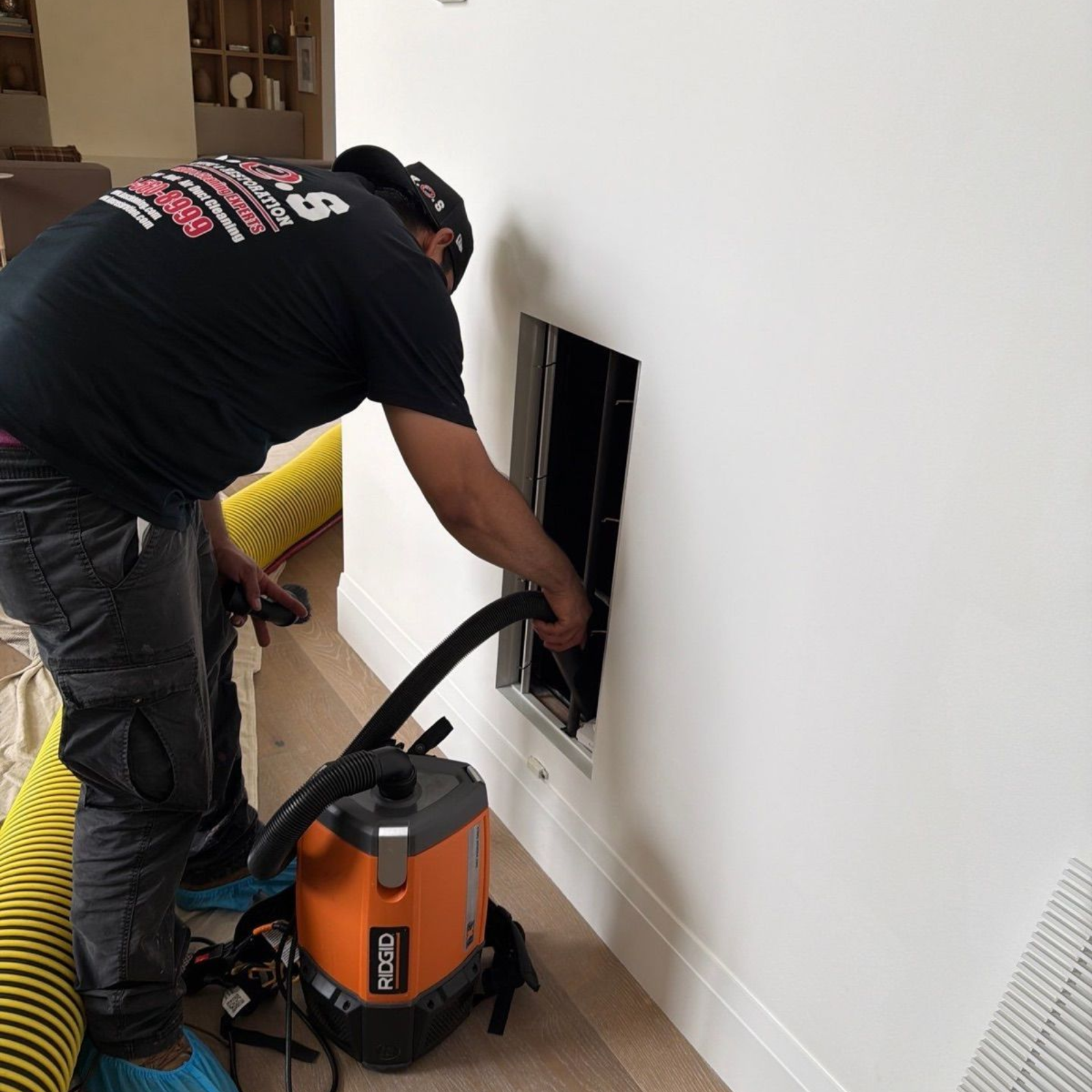 Worker using a shop vacuum to clean drywall dust from a wall opening in a room under renovation