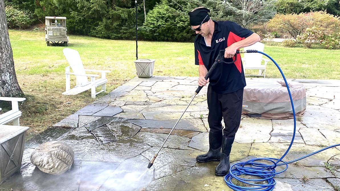 Technician power washing a patio to prep a Suffolk County home for summer