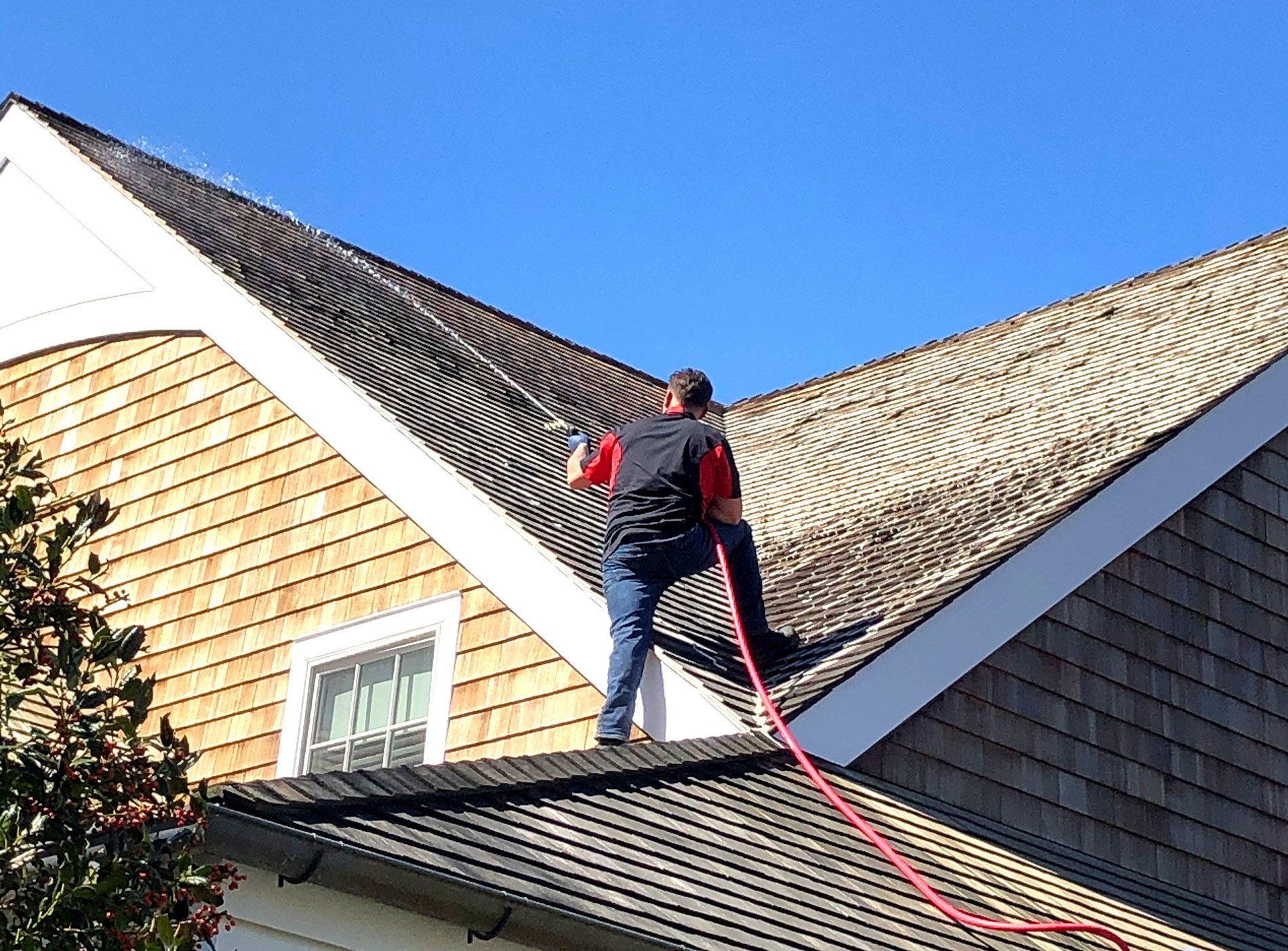 a man is cleaning the roof of a house with a hose