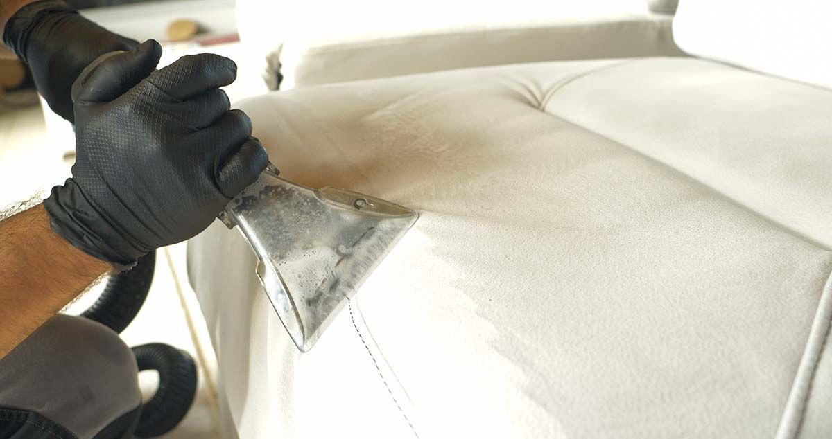 A upholstery technician is cleaning a dirty couch at a home on Long Island. 
