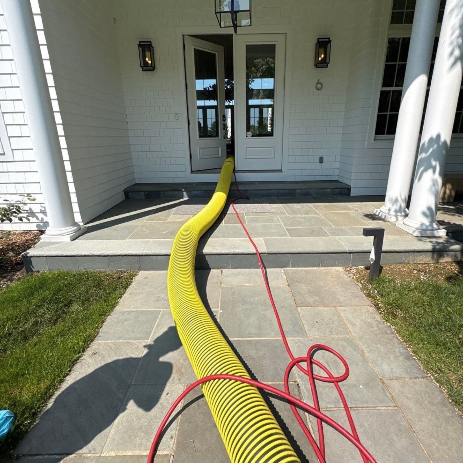 Yellow hose or cable across a front walkway leading to a white house entryway