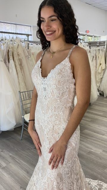 Woman in a white lace wedding dress, smiling, in a bridal shop.