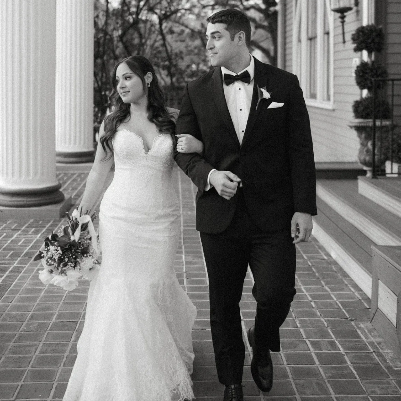 Bride and groom walking, arm in arm, near columns, smiling. Black and white.