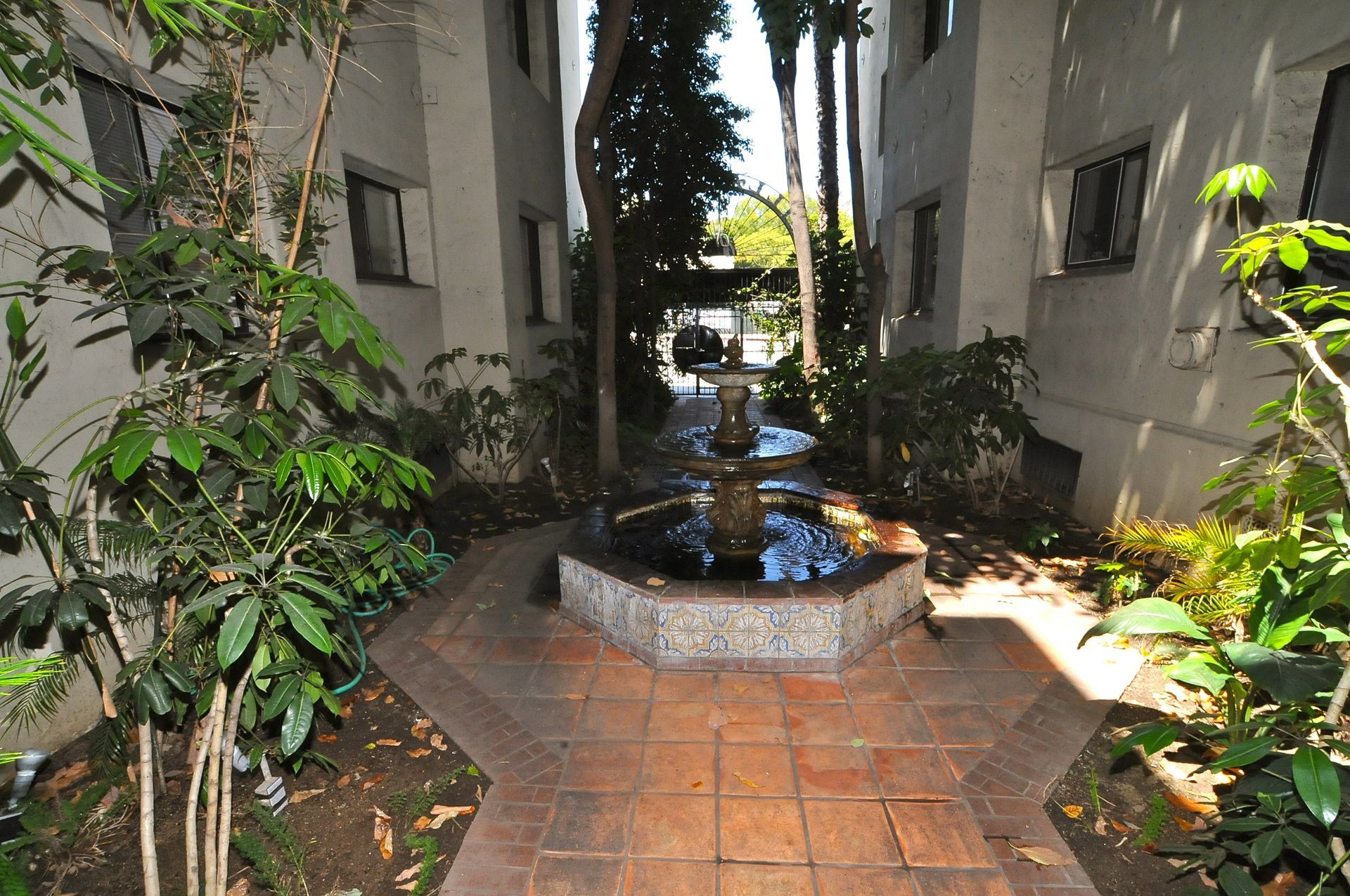 Courtyard with fountain, surrounded by buildings and greenery. Brick path.