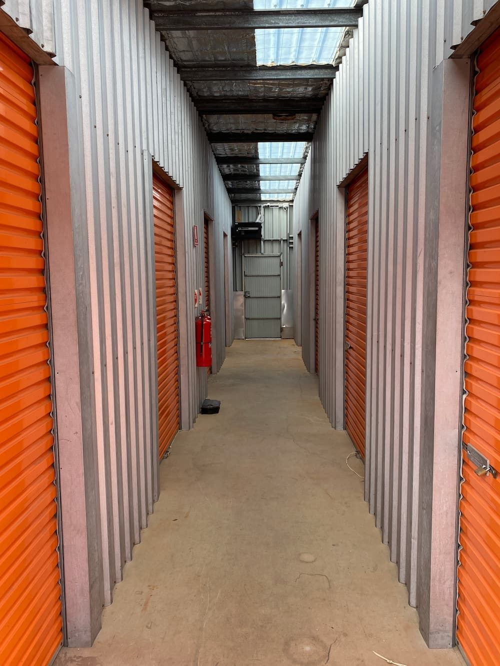 A Long Hallway With Orange Doors And A Red Fire Extinguisher — Acacia Mini Storage in Port Macquarie, NSW