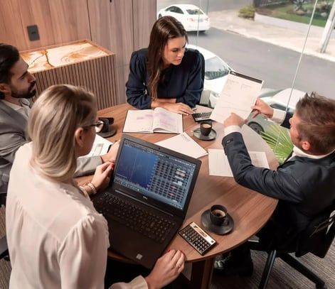 Um grupo de pessoas está sentado ao redor de uma mesa com laptops.