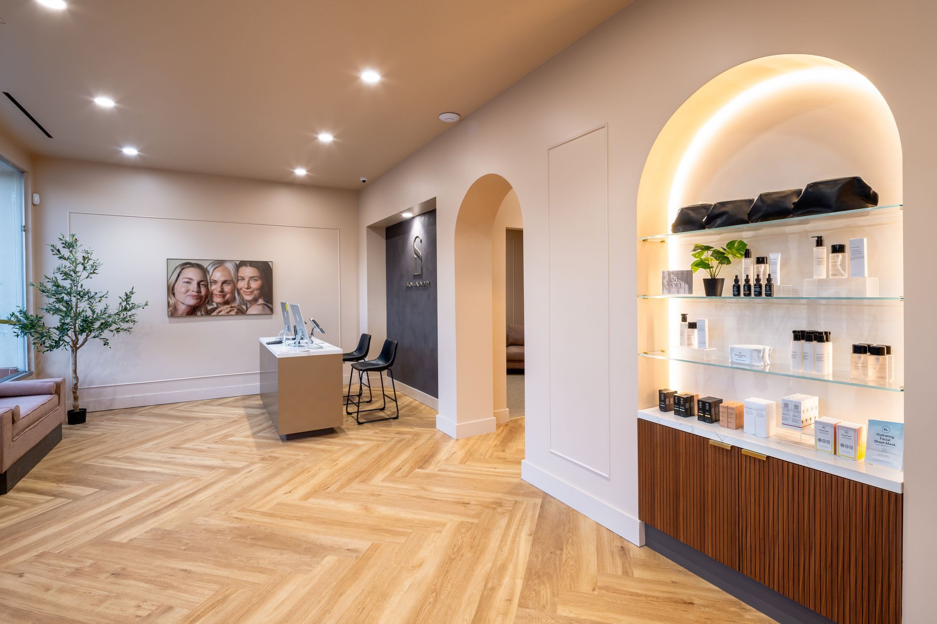 Modern clinic reception with wood floors, arched display niche, and warm recessed lighting