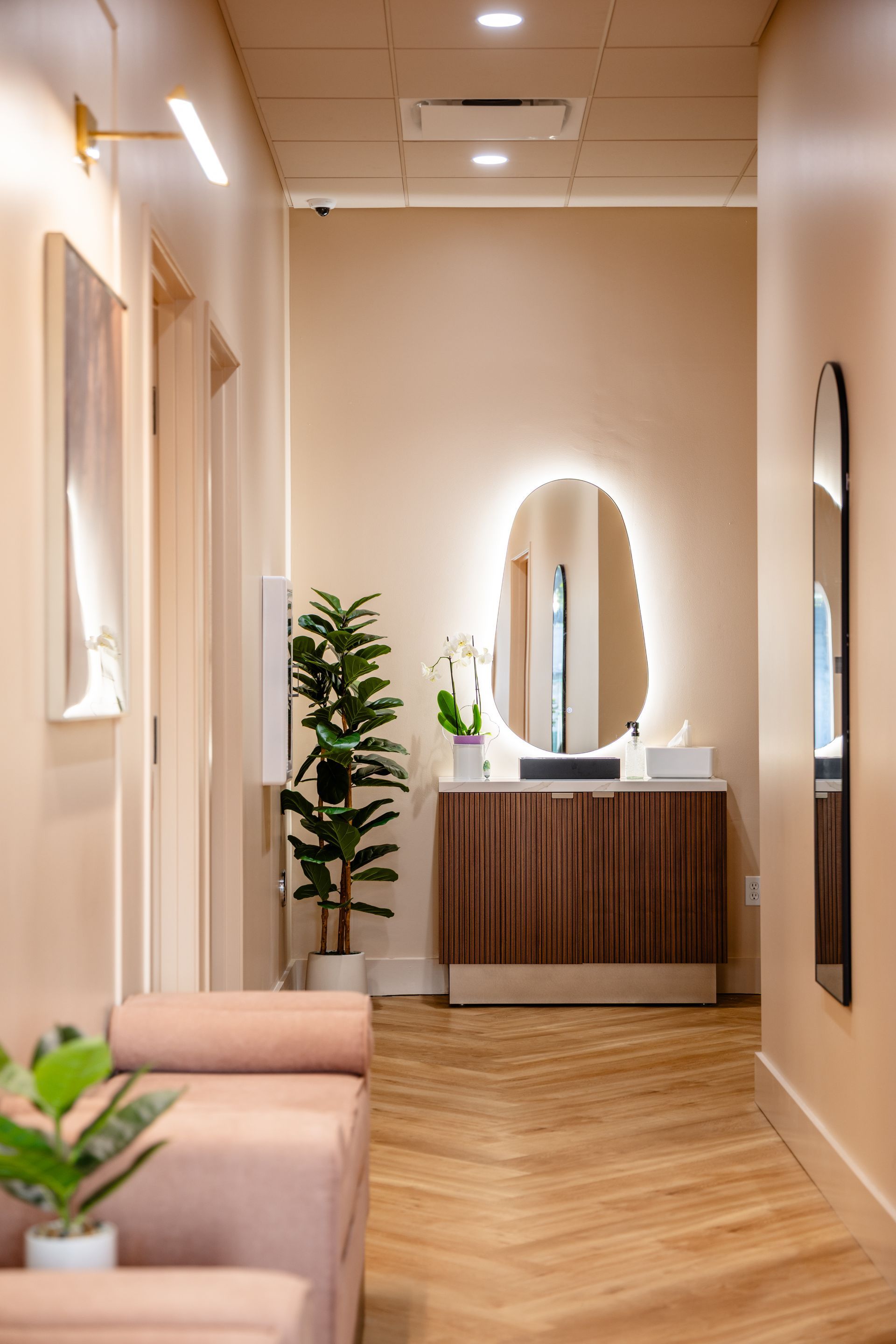 Elegant spa hallway with beige walls, wood flooring, mirrors, and a vanity sink under warm lighting