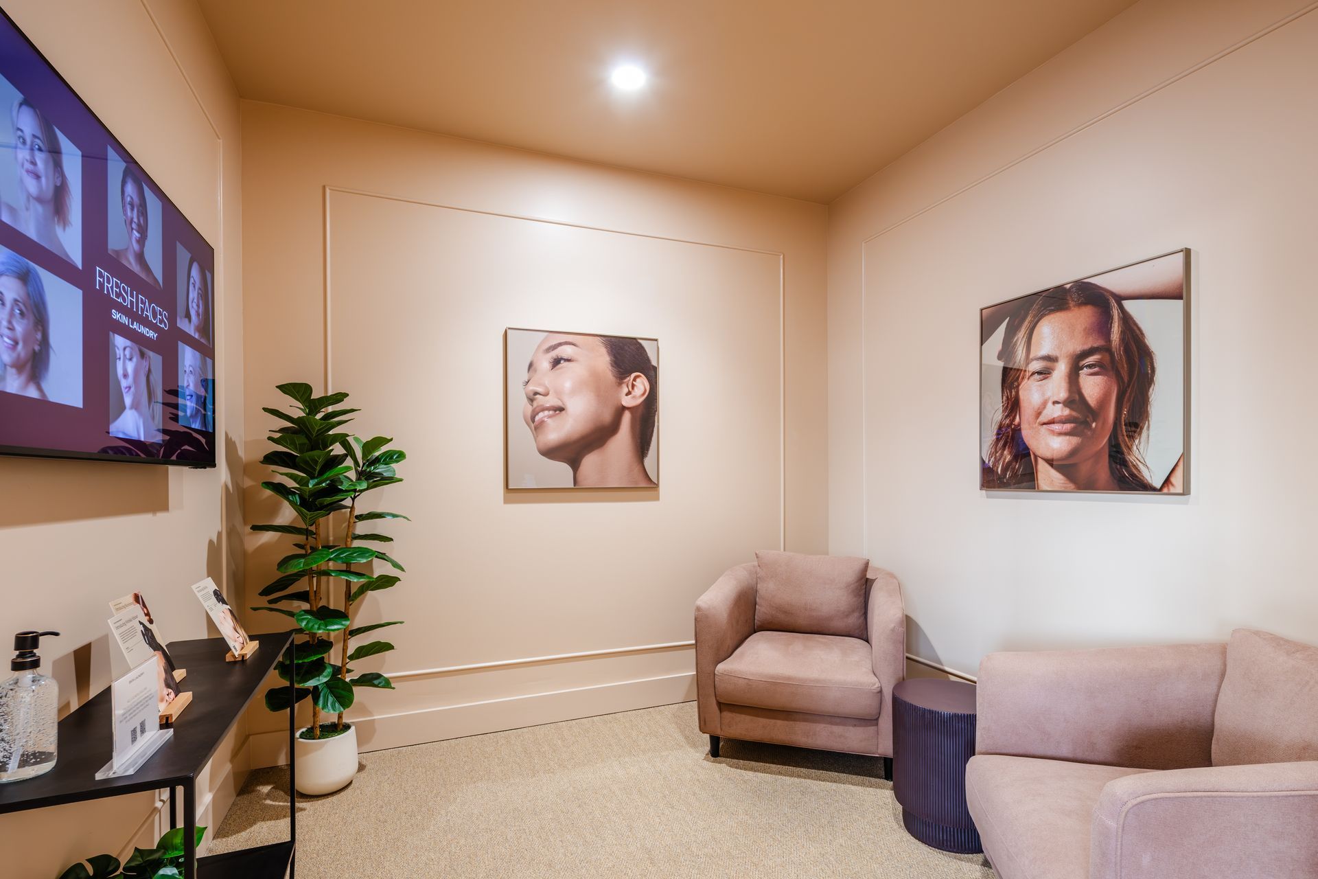 Modern waiting room with beige walls, armchairs, potted plant, and framed portraits of smiling faces