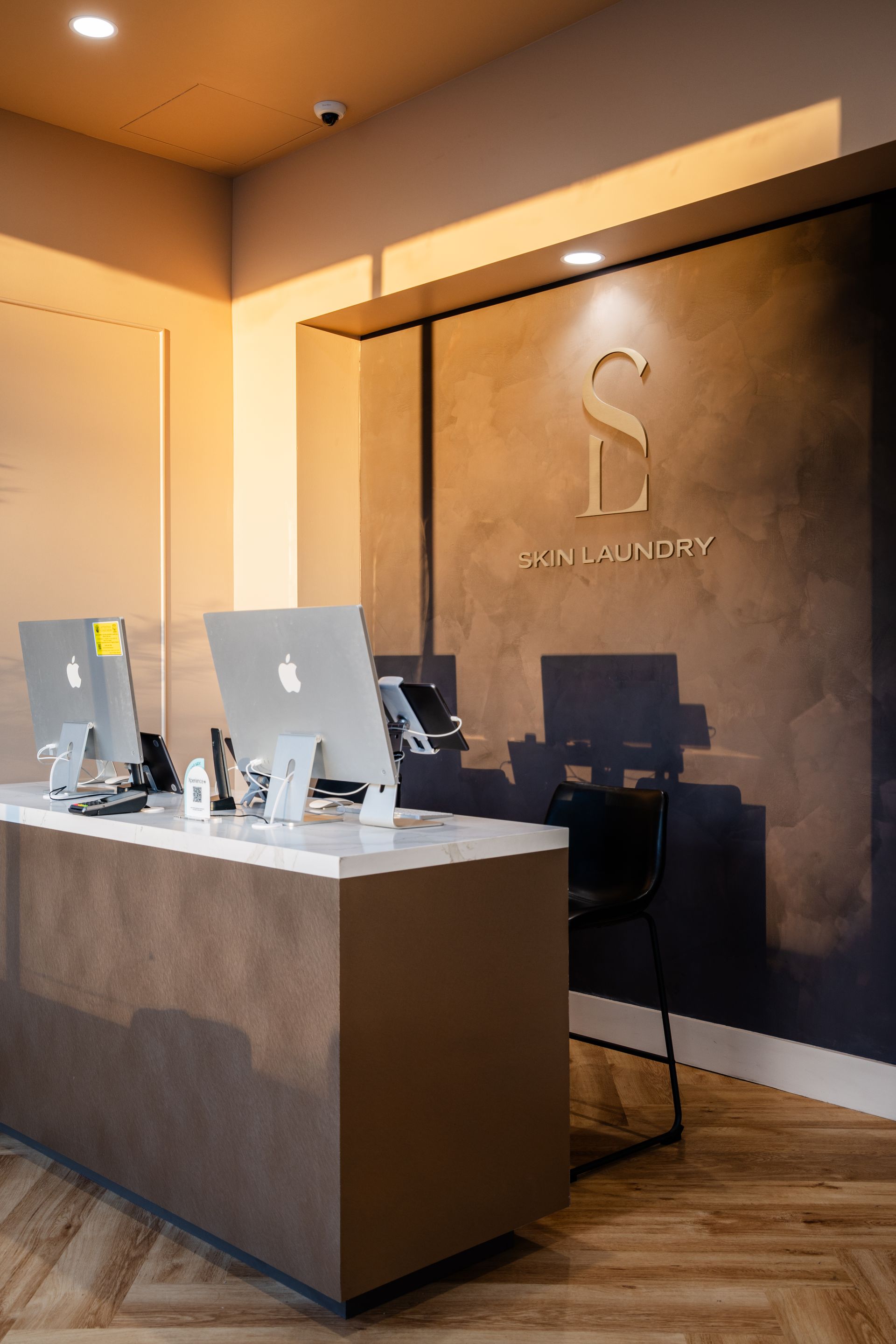 Modern reception desk in a warmly lit lobby with a dark accent wall and logo signage.