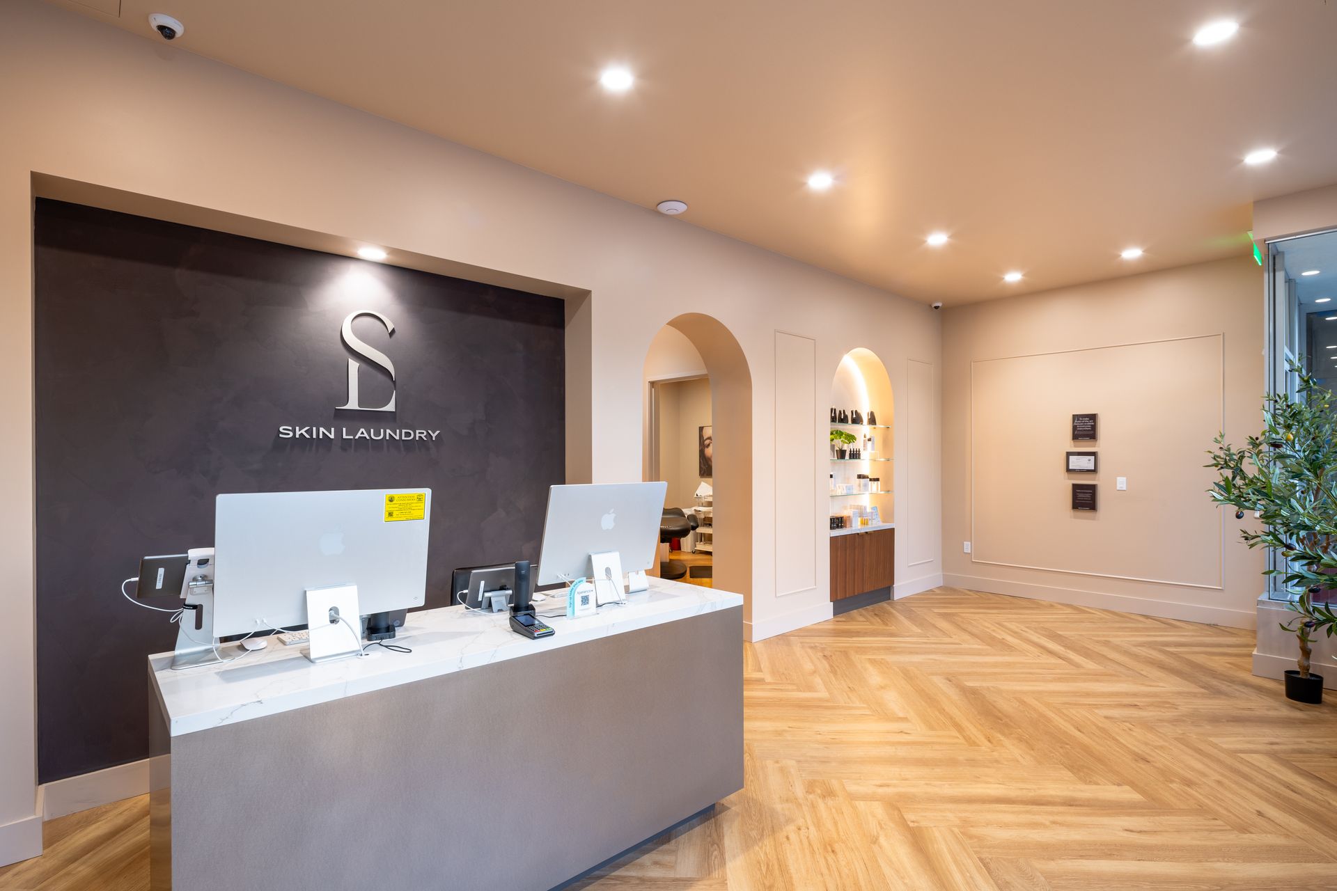 Modern reception desk in a beige lobby with wood floors, recessed lights, and arched doorways
