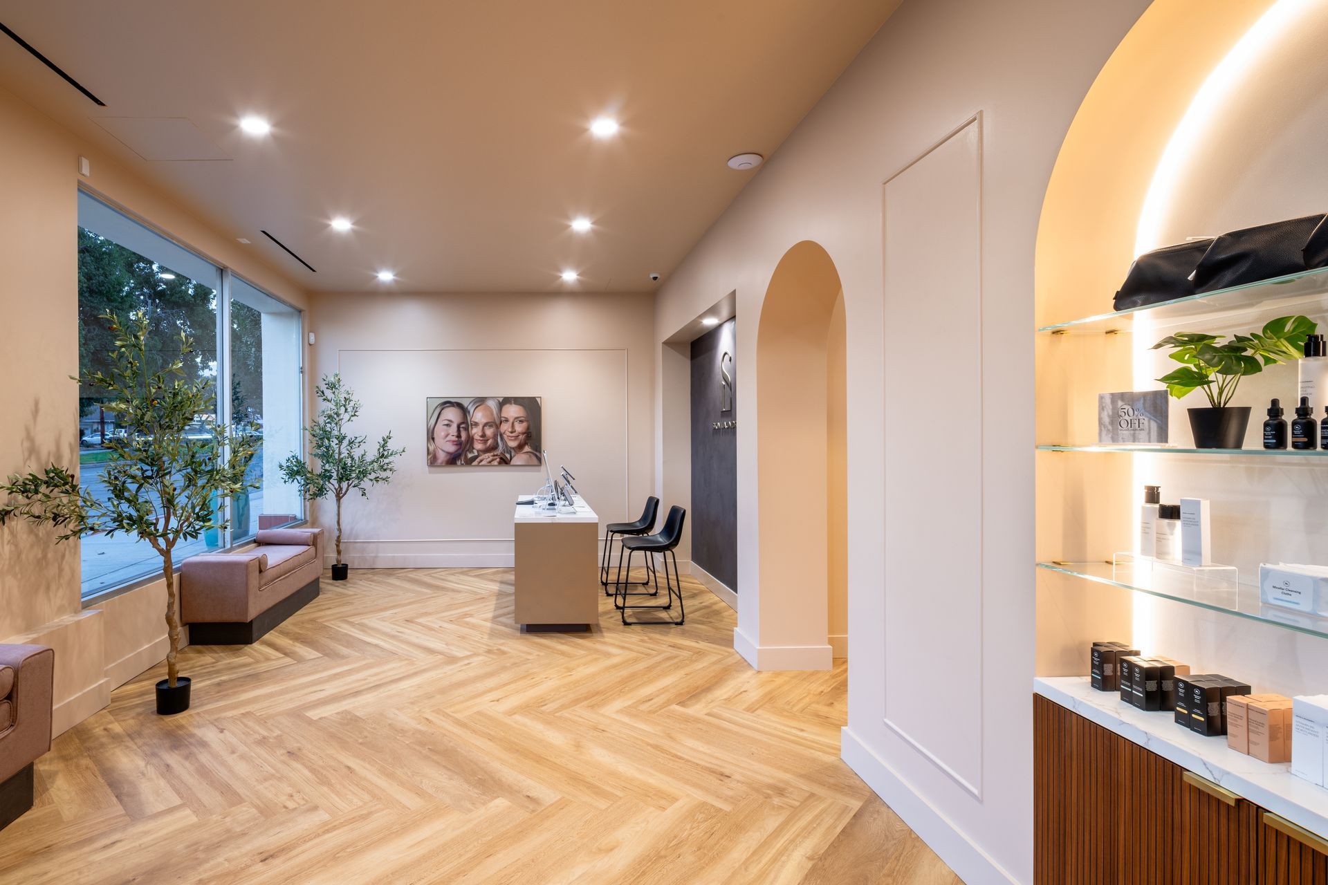 Bright modern office lobby with herringbone wood floors, arched doorway, and reception desk near a large window.