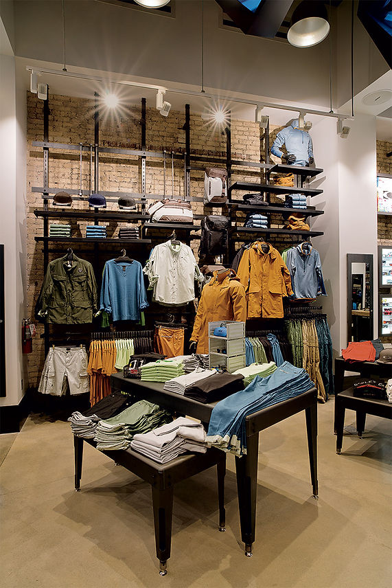 Clothing store interior with shelves of folded shirts and hanging jackets on display tables and racks