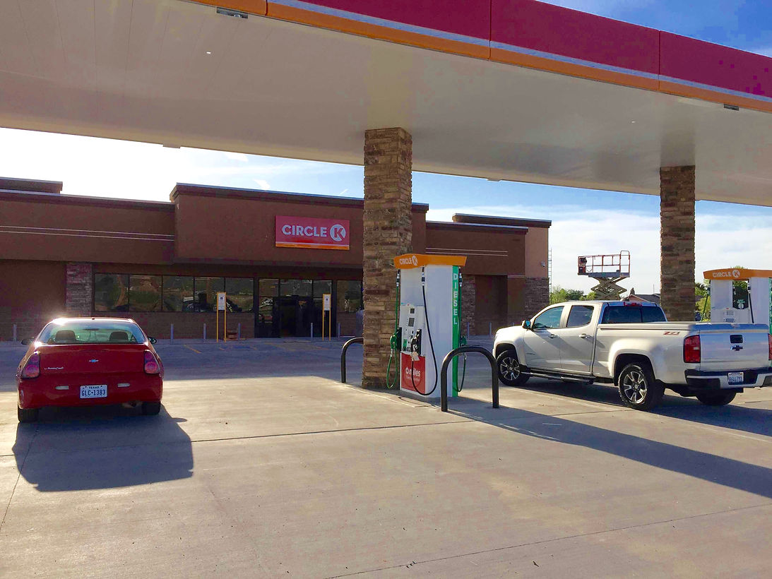 Gas station forecourt with a red car, white pickup, and pumps under a canopy
