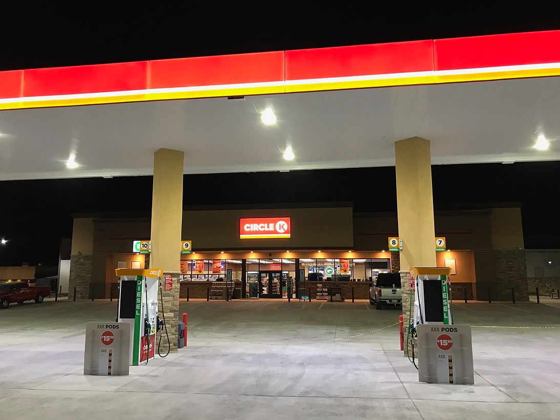 Gas station convenience store at night with bright red-lit sign and two pumps under a canopy