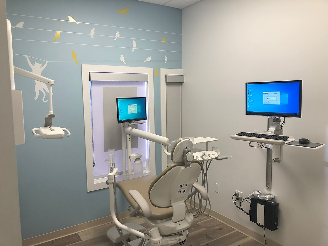 Dental exam room with chair, mounted monitor, and dental equipment in a blue and white setting