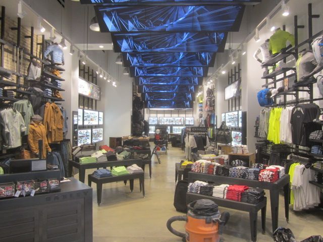 Clothing store interior with racks of outdoor apparel and blue-lit ceiling displays