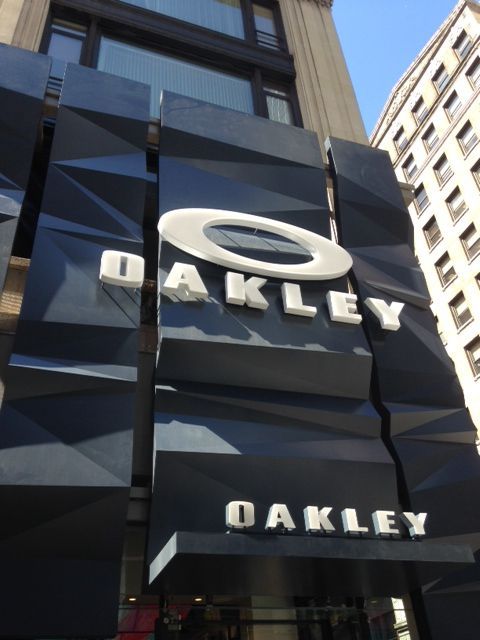 Oakley storefront with large white logo on a dark glass facade in a city setting
