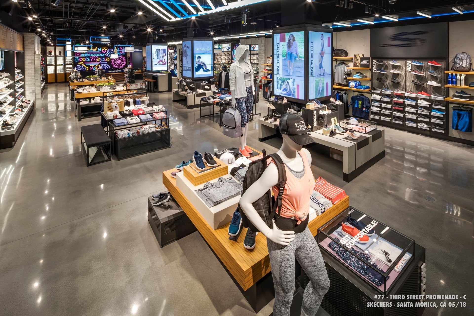 A modern shoe store interior with display tables, shelves, and mannequins under bright overhead lights.