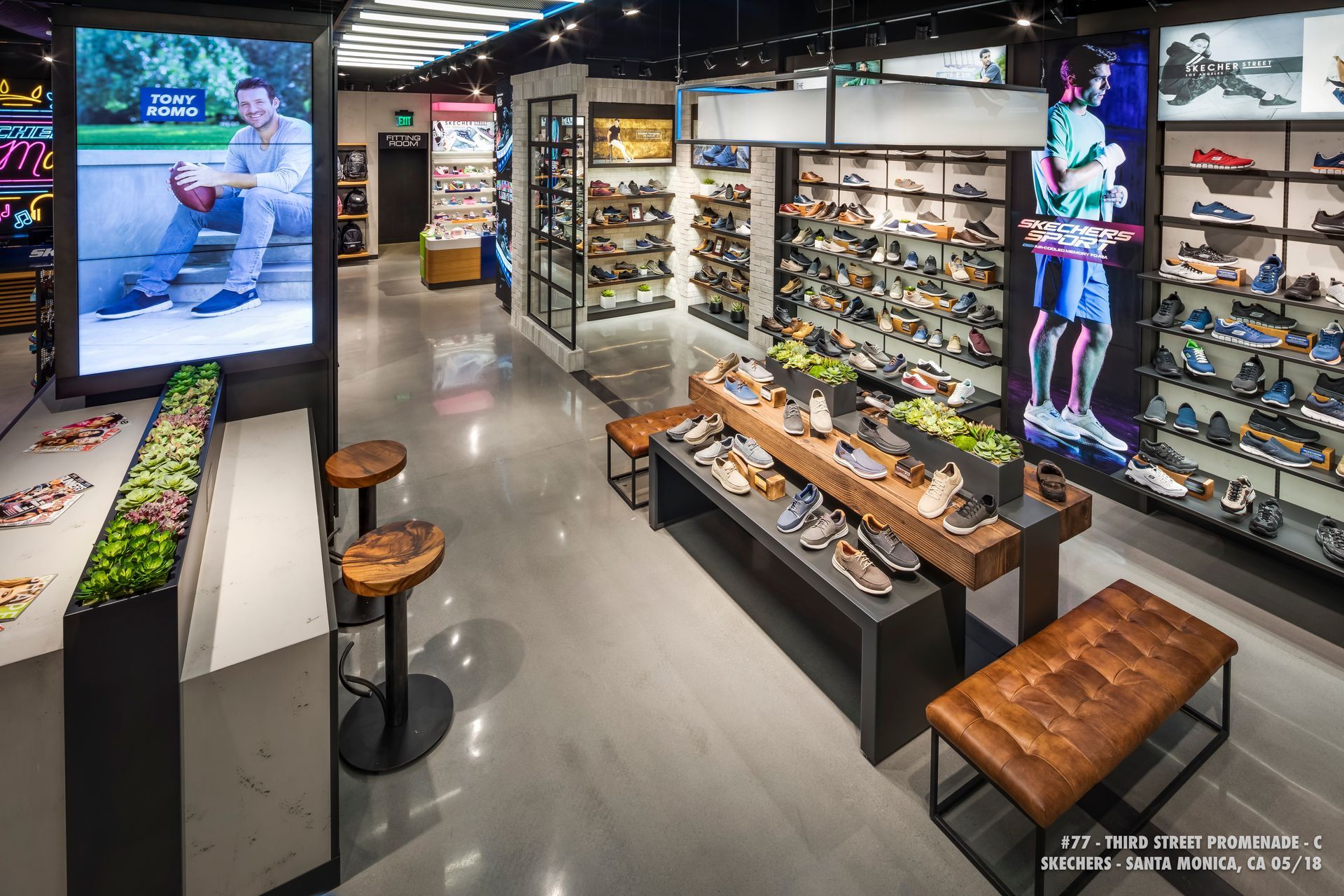 Shoe store interior with rows of sneakers, display shelves, and a large digital ad screen