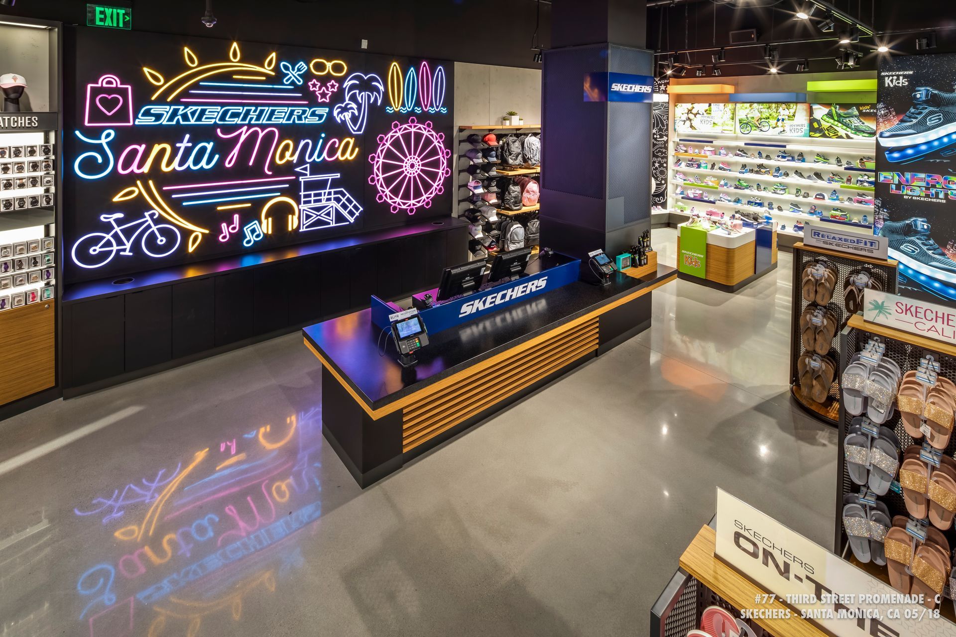 Neon “Santa Monica” sign in a modern store aisle with shelves, a display table, and polished floor reflections