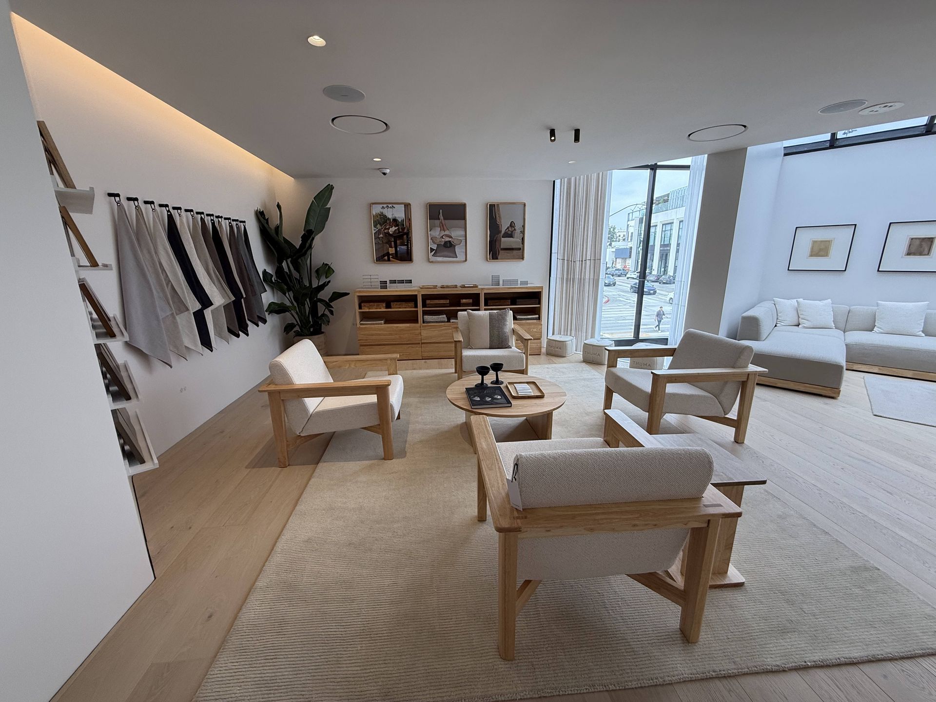 Modern living room with beige chairs, a rug, wall art, and large windows overlooking a city.