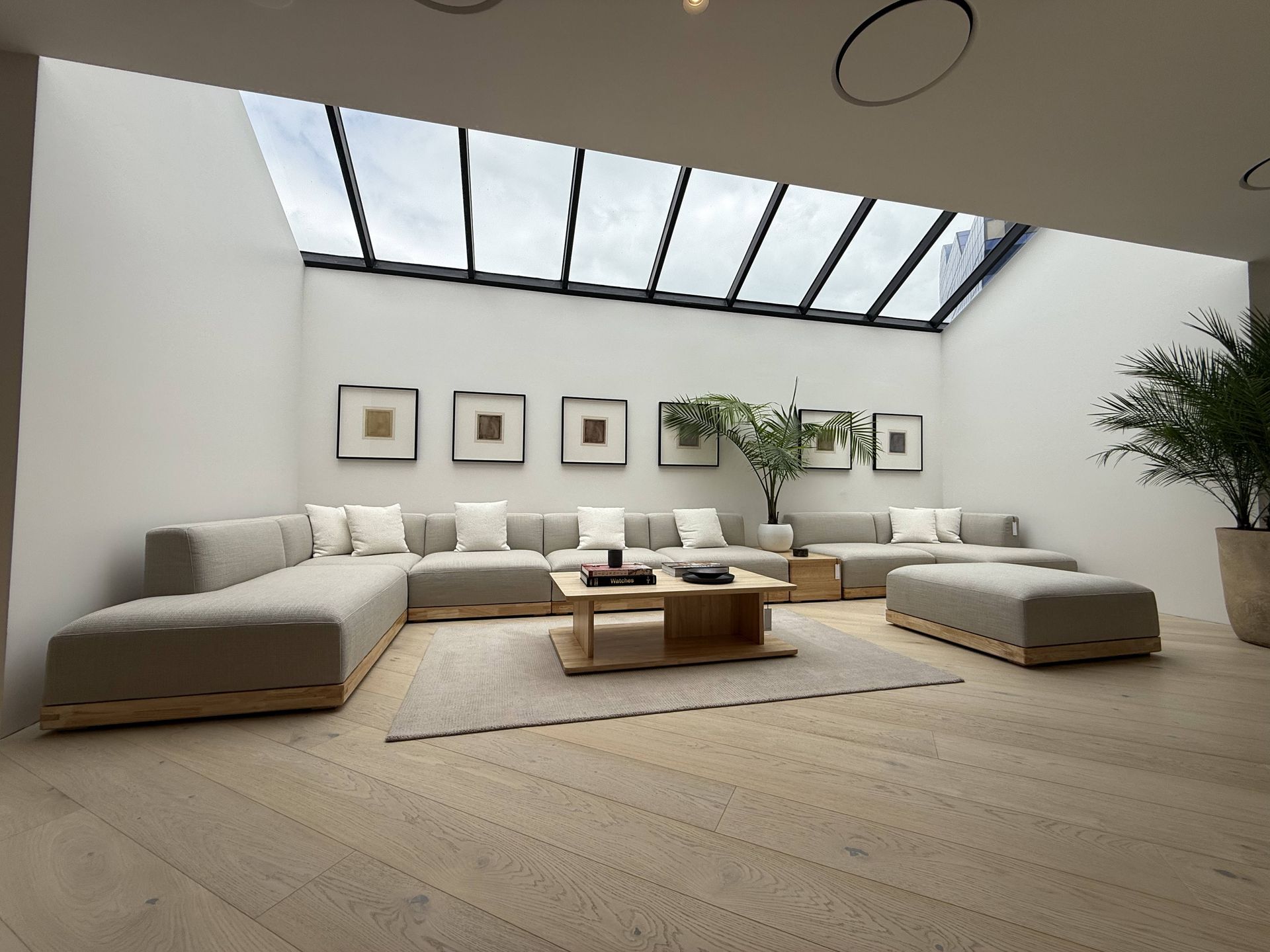 Bright minimalist living room with low beige sofas, skylight, wall art, plants, and a coffee table