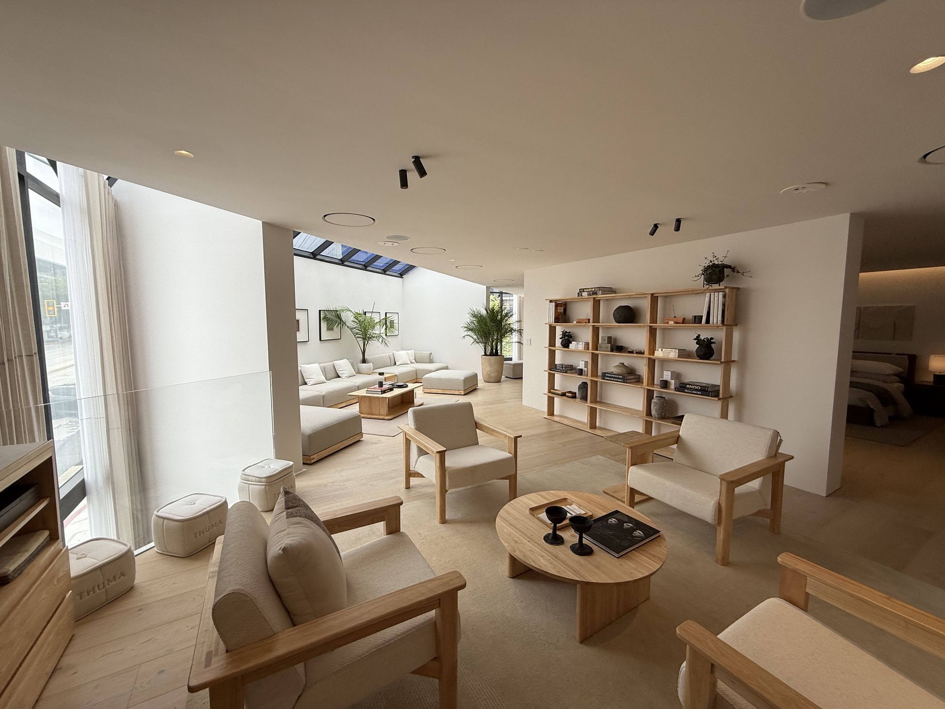 Bright modern lounge with wooden chairs, low tables, shelves, and large windows with city views