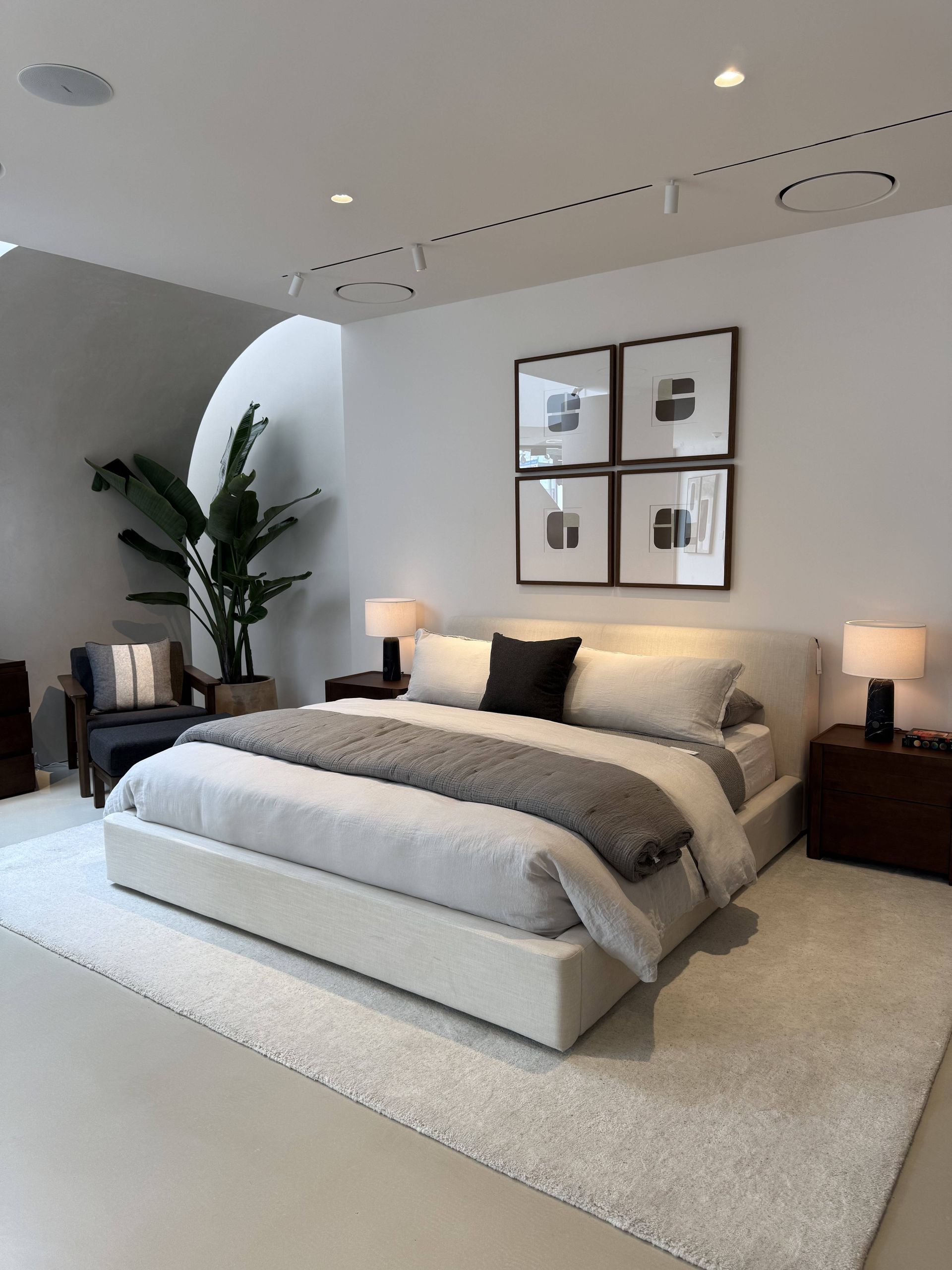Modern bedroom with a low white bed, beige bedding, nightstands, lamps, and framed wall art.