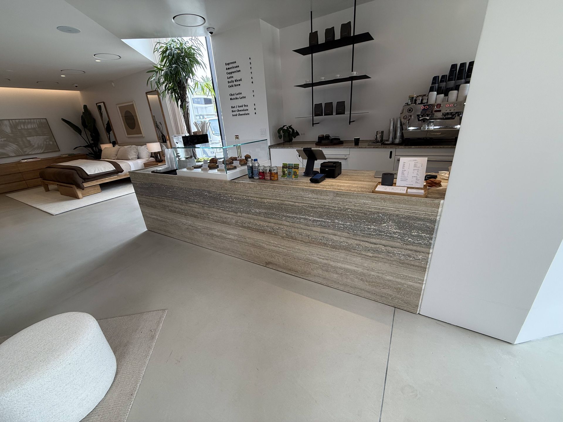 Modern minimalist café interior with a marble counter, shelves, plants, and soft neutral furnishings.