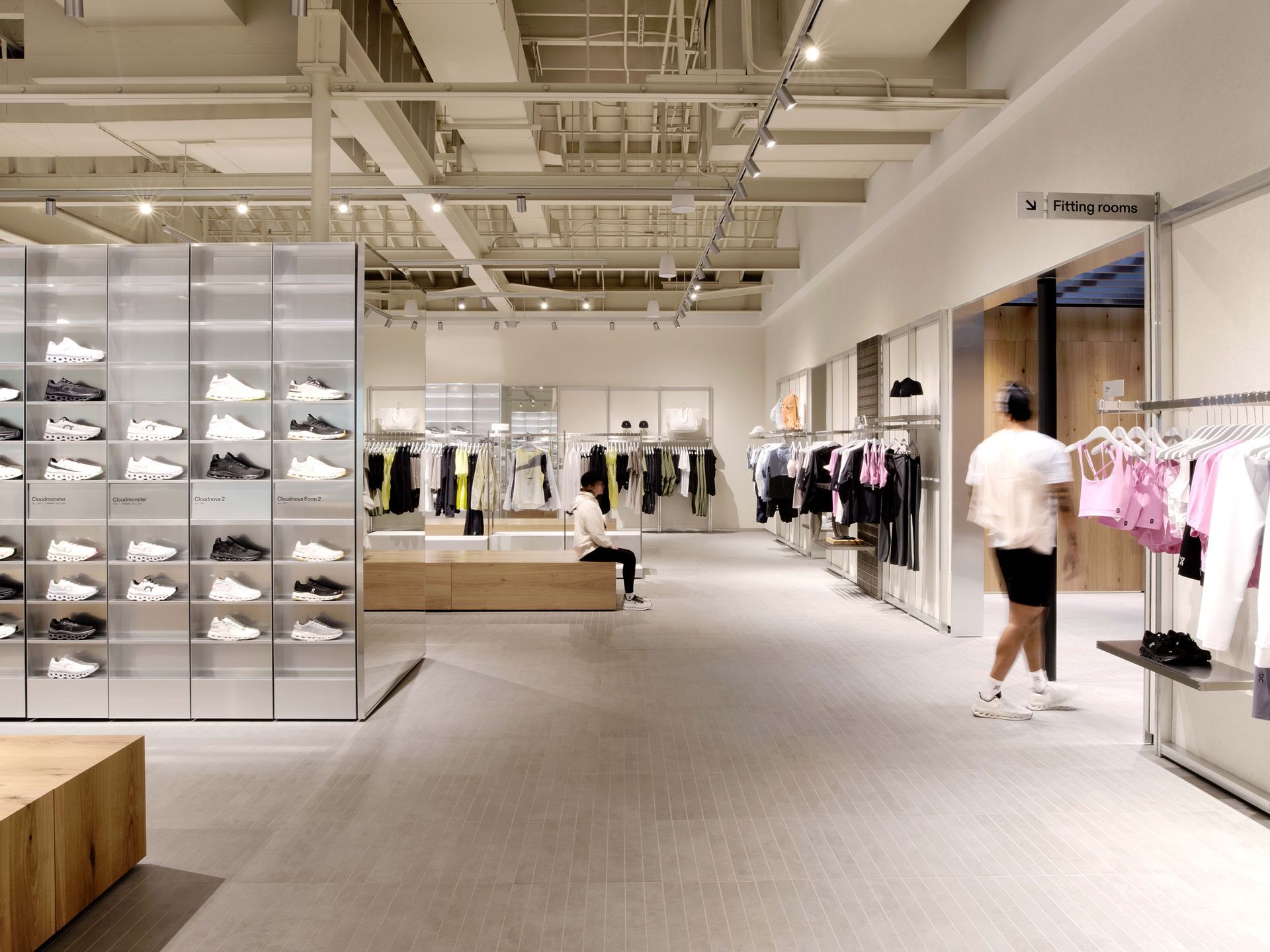 Bright clothing store interior with racks, shelves, and a few shoppers browsing.