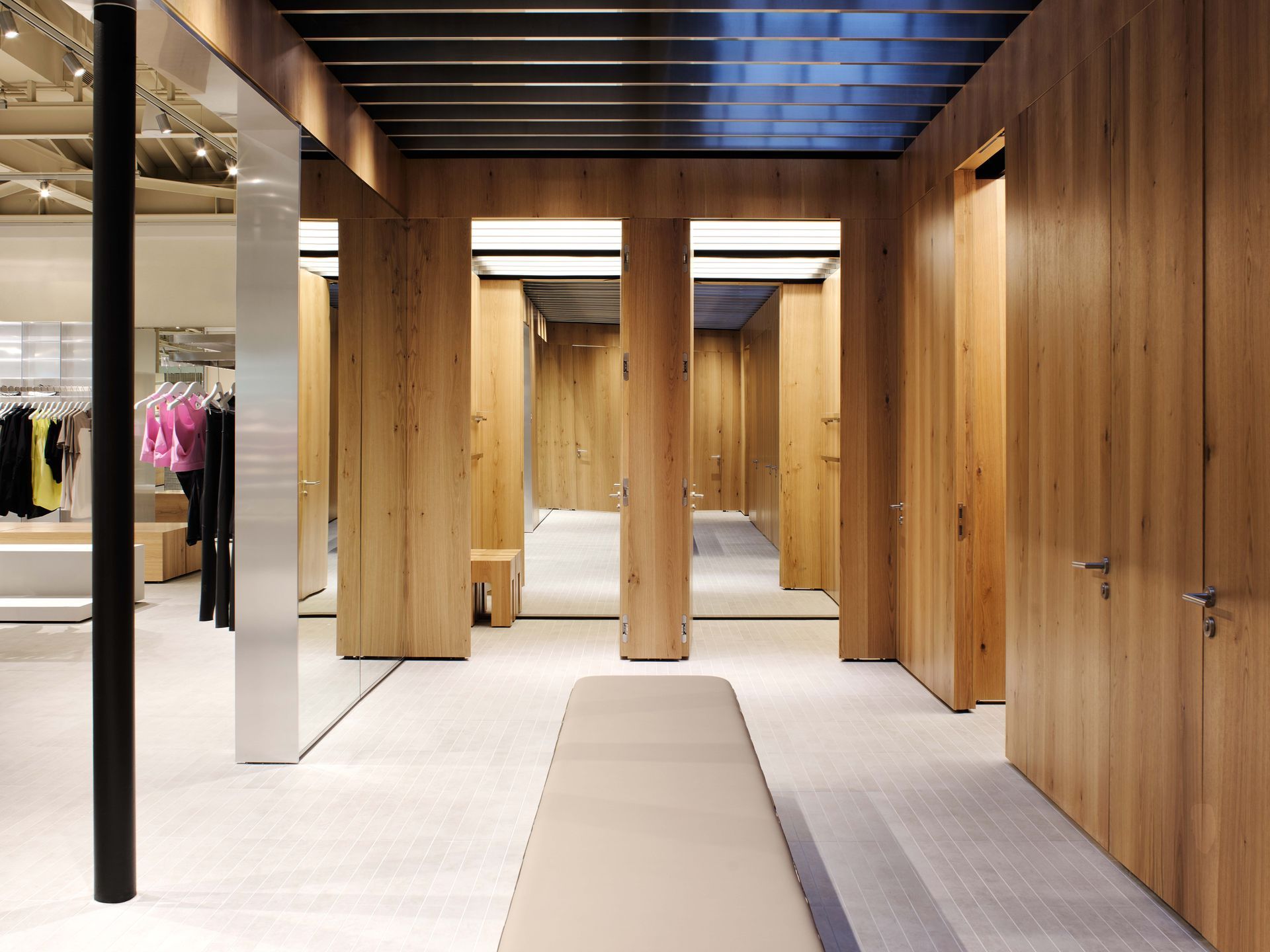 Modern clothing store fitting area with wood-paneled stalls and a central bench under dark ceiling beams