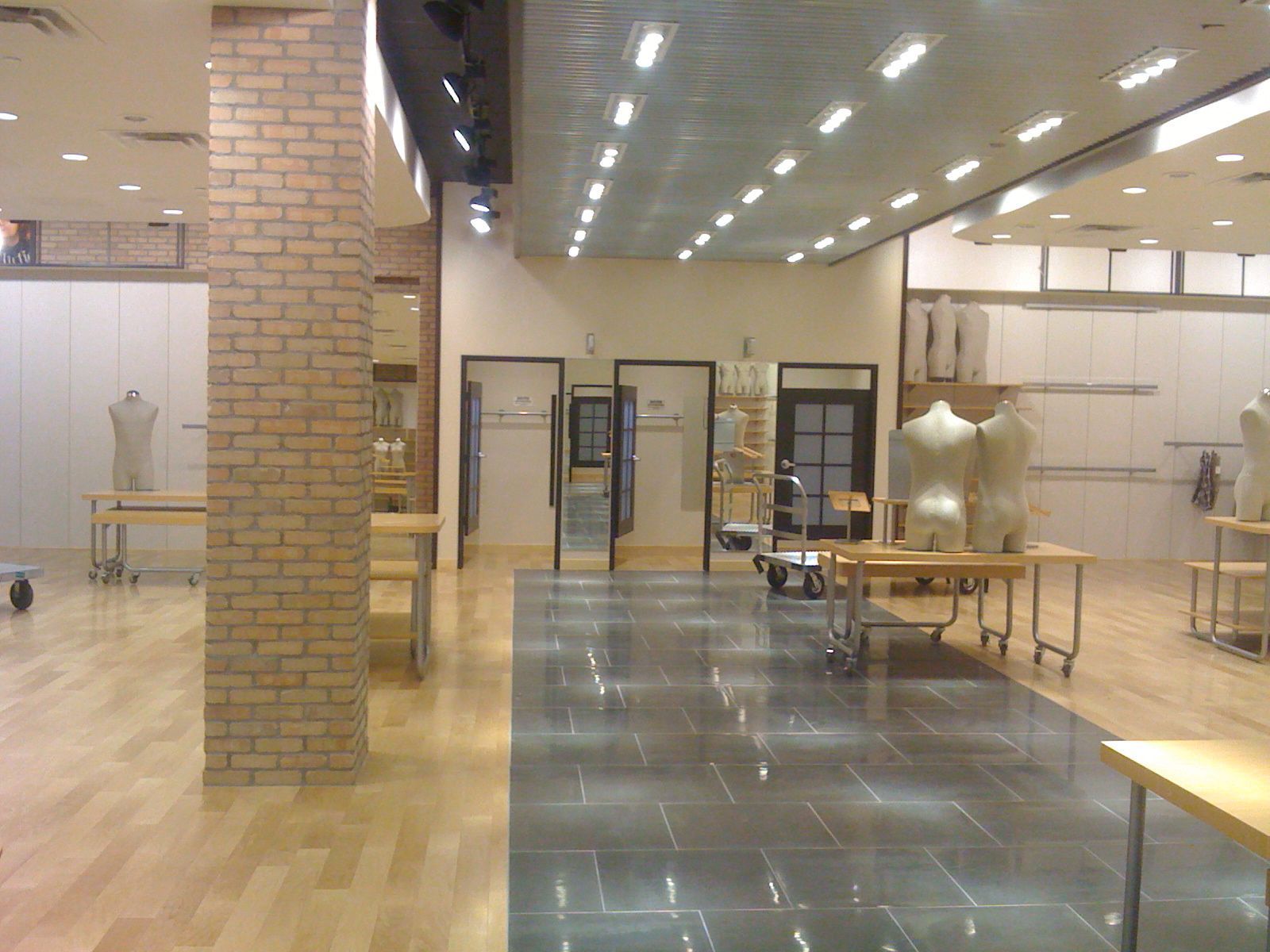 Empty modern lobby with brick columns, wood floors, glass doors, and tables under bright ceiling lights