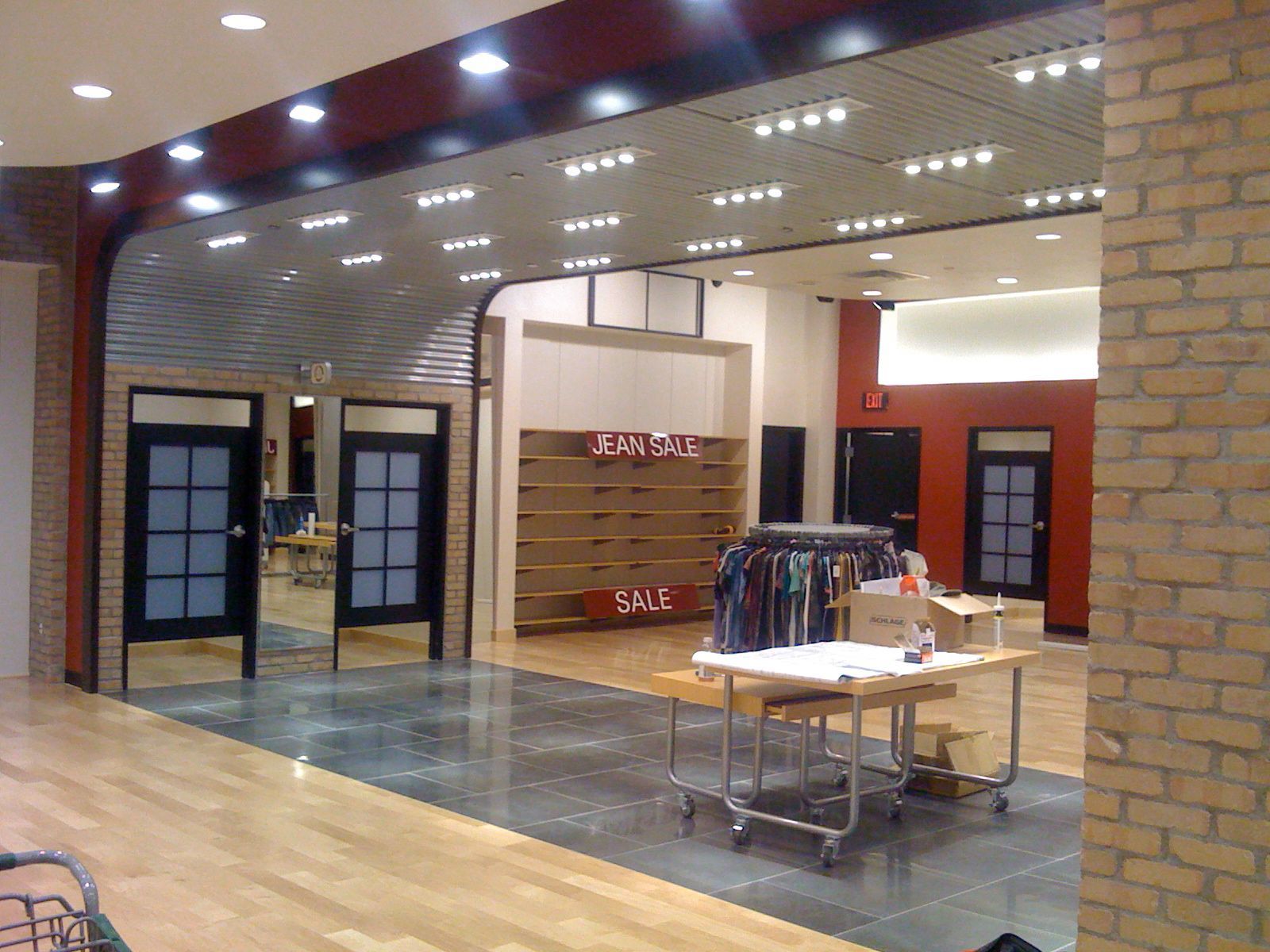Empty clothing store with racks, tables, and sale signs inside a mall corridor