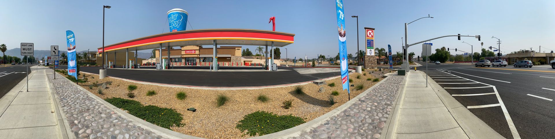 Wide-angle view of a gas station and road intersection on a sunny day with blue signs and traffic lights