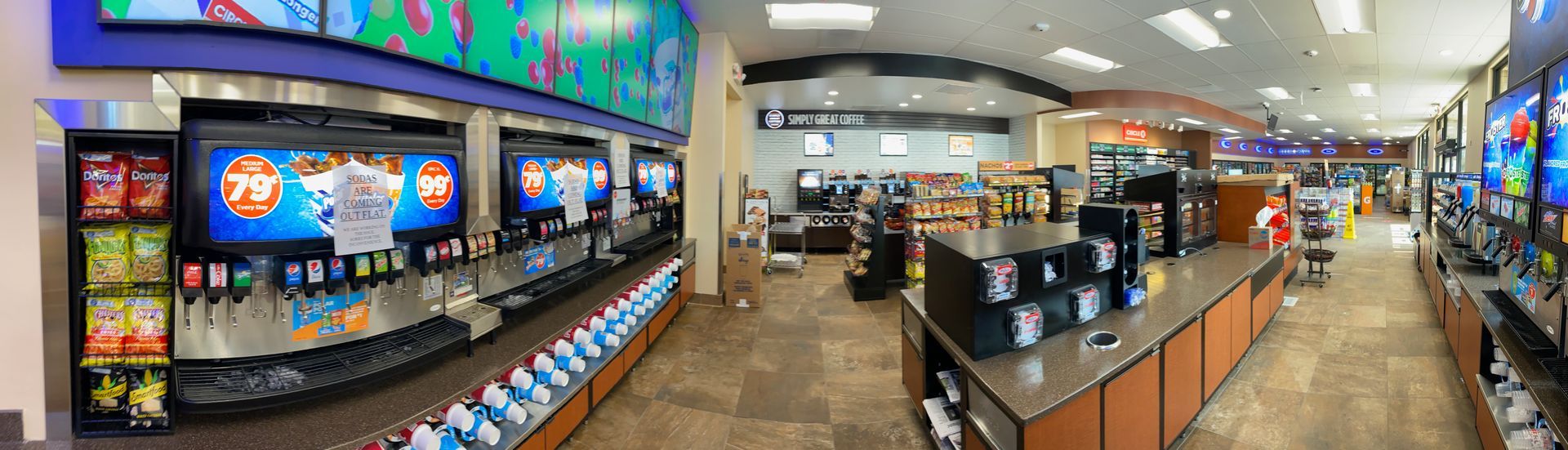 Bright arcade with colorful game machines, counters, and overhead TV screens inside a gaming venue