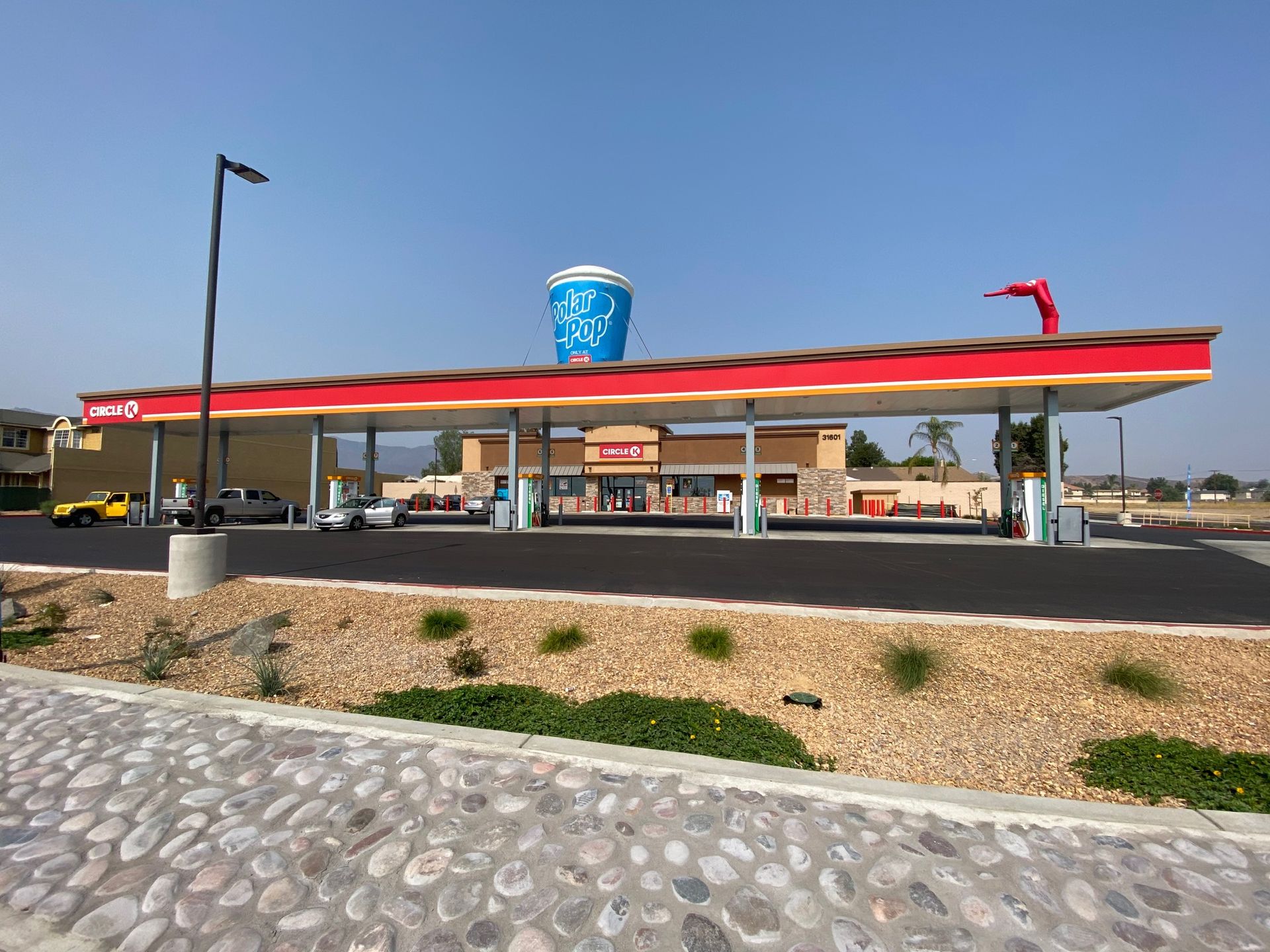 Gas station with red canopy and blue sign beside a cobblestone path under a blue sky