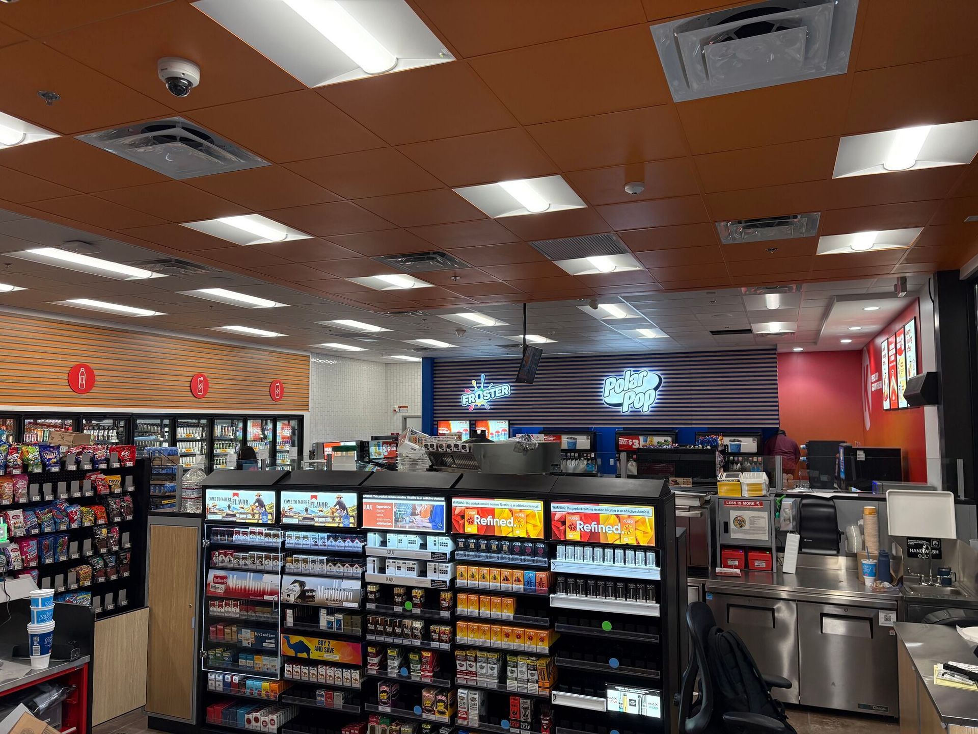 Convenience store interior with snack aisles, coolers, and a coffee station under bright ceiling lights