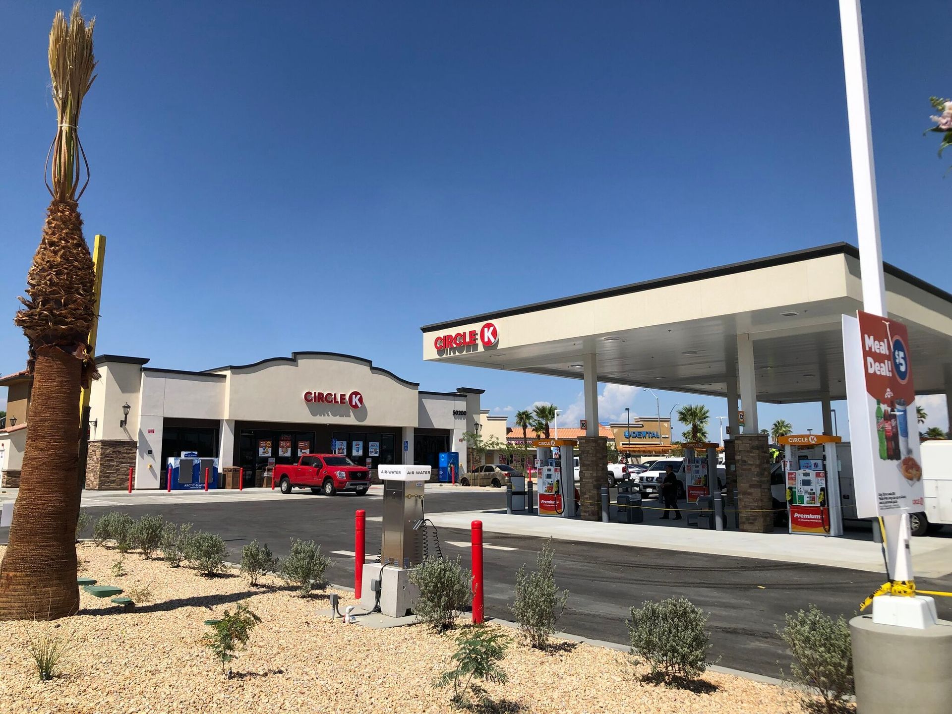 Valero gas station with canopy, pumps, and parked cars under a clear blue sky.