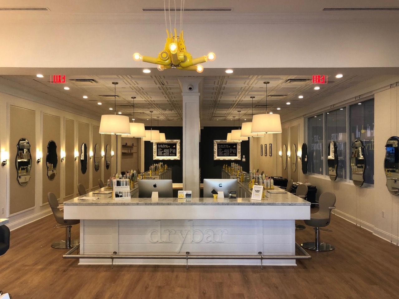 Elegant salon interior with white reception desk, mirrors, pendant lights, and brown wood floors.