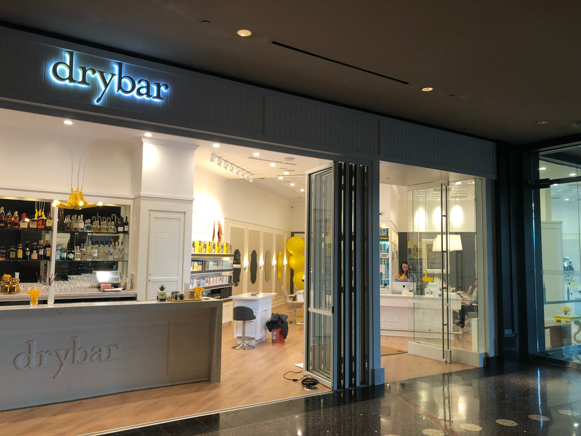 Drybar salon storefront with lit sign, glass entrance, and product shelves inside