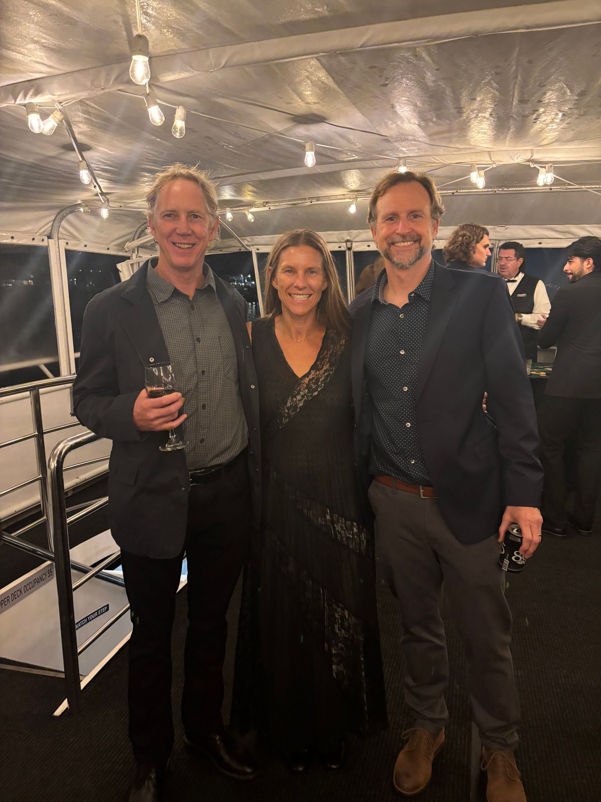 Three people posing and smiling at a nighttime event under a lit tent.