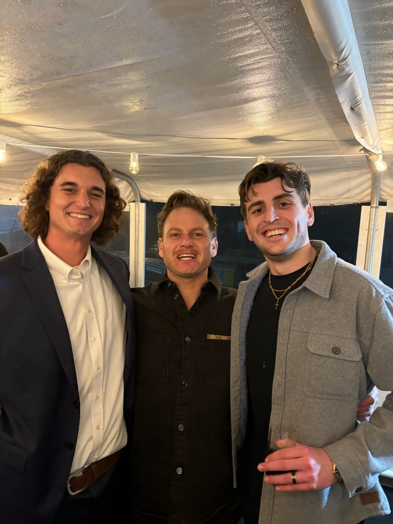 Three smiling people standing together under a white tent at an event.