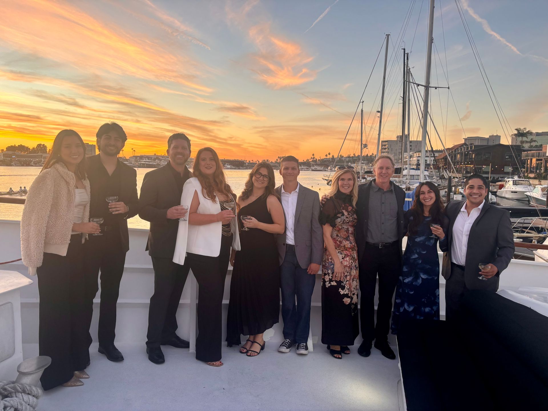 Group of people posing on a dock at sunset, with boats and sailboat masts in the background.