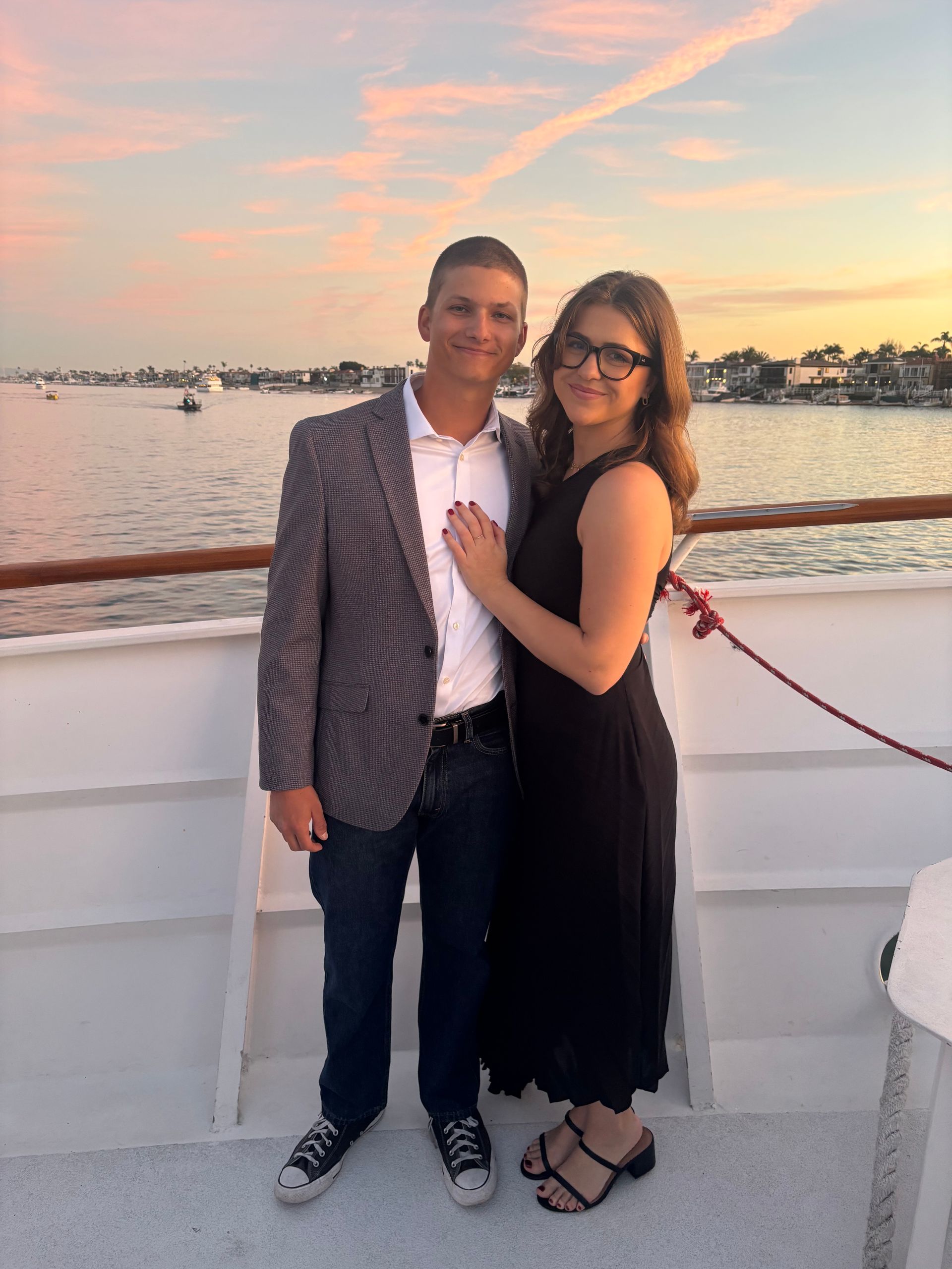 Couple posing on a boat deck at sunset, with water and pastel sky in the background.