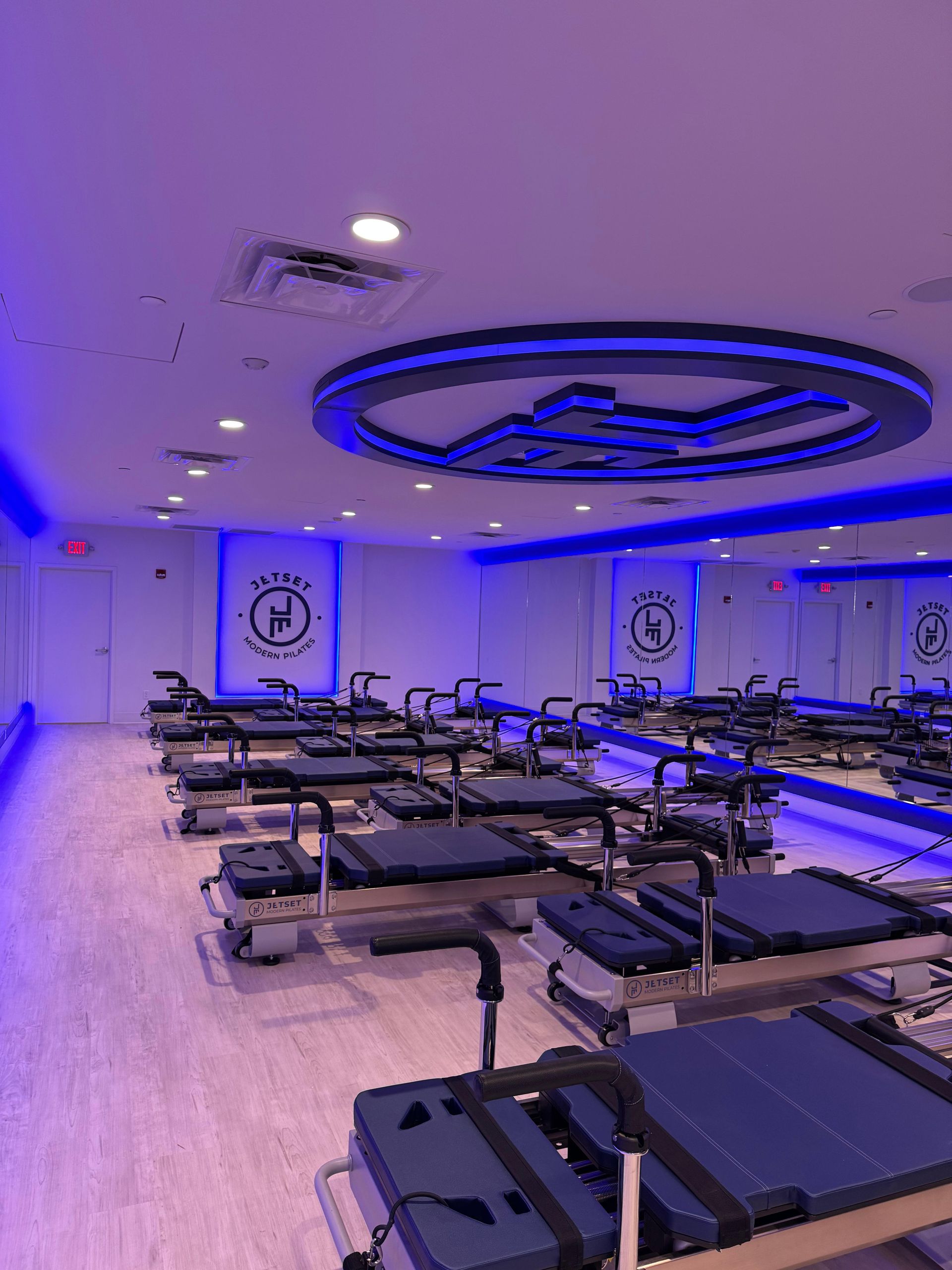 Blue-lit Pilates studio with rows of reformer machines and mirrors