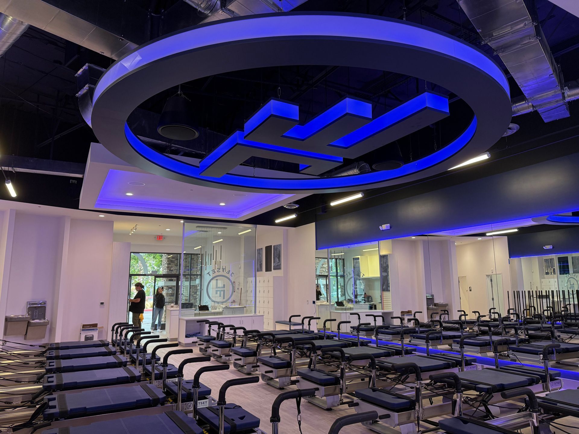 Empty gym with rows of bikes and a large blue neon ceiling logo.