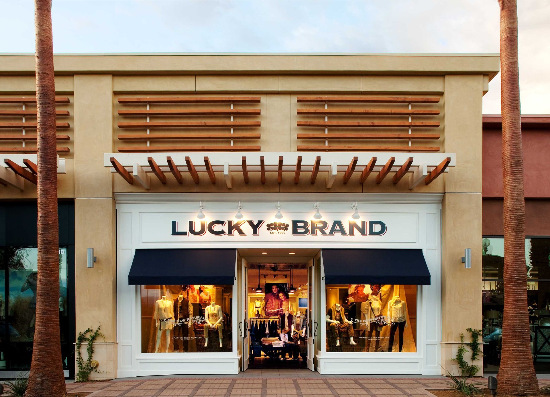 Storefront of Lucky Brand with a blue awning and clothing displays in the windows.
