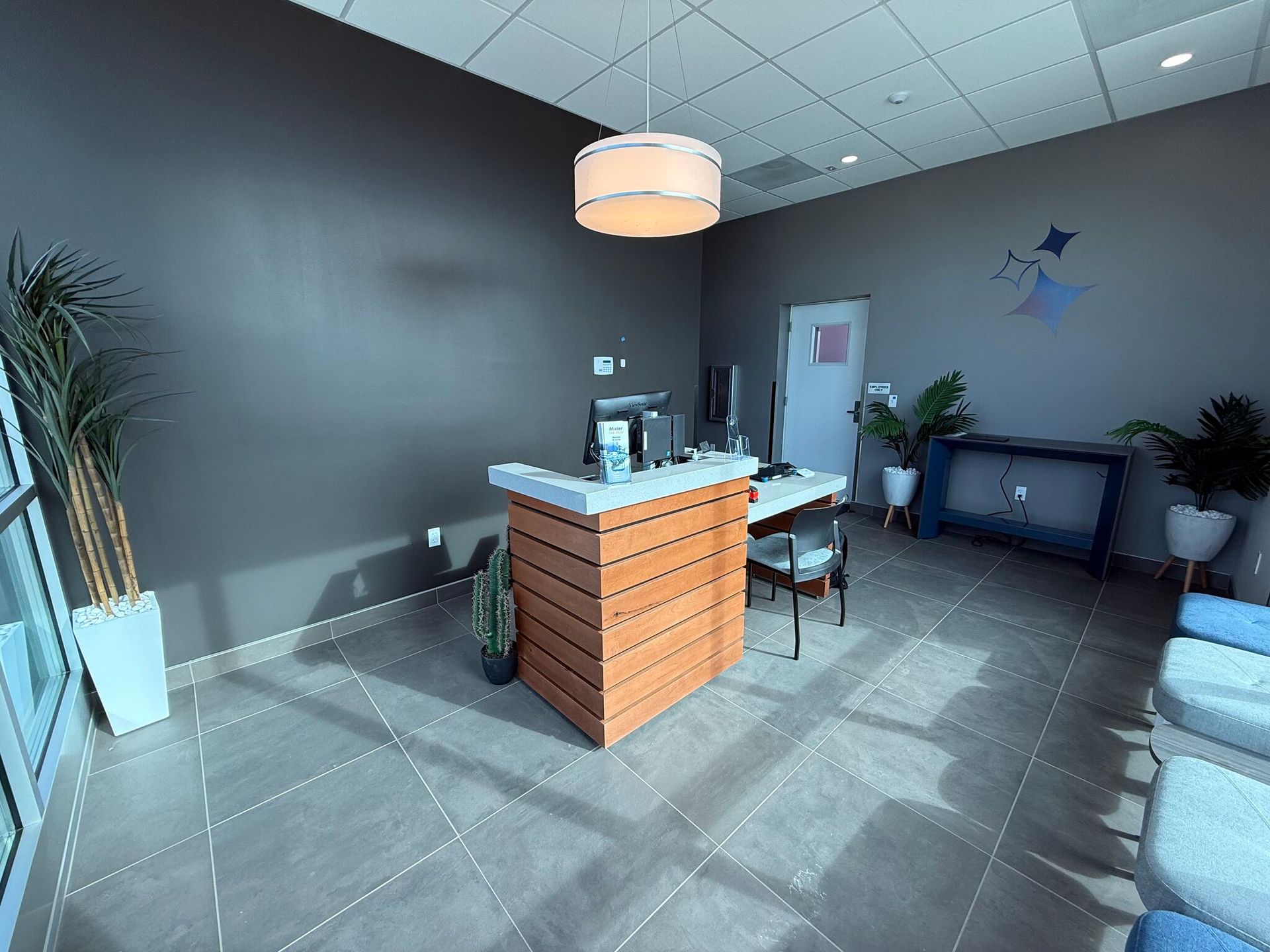 Modern lobby with wood reception desk, gray walls, pendant light, and seating area