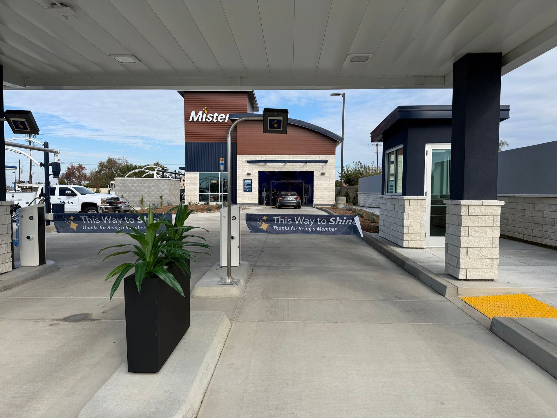 Drive-through entrance to a bank with barriers, a potted plant, and a building ahead under a covered canopy.